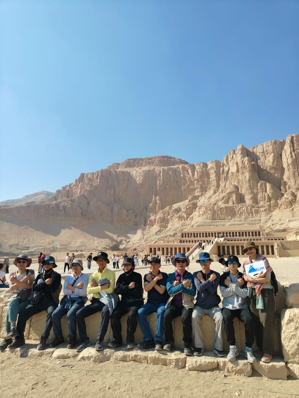 Tour group seated on a wall striking the pharaoh pose in front of the Temple of Hatshepsut